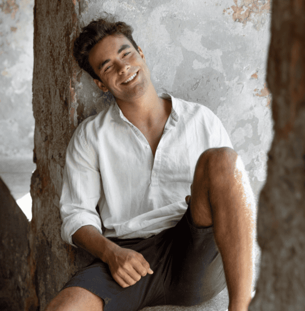 Homme portant une chemise blanche avec short, look estival décontracté et élégant assis en extérieur