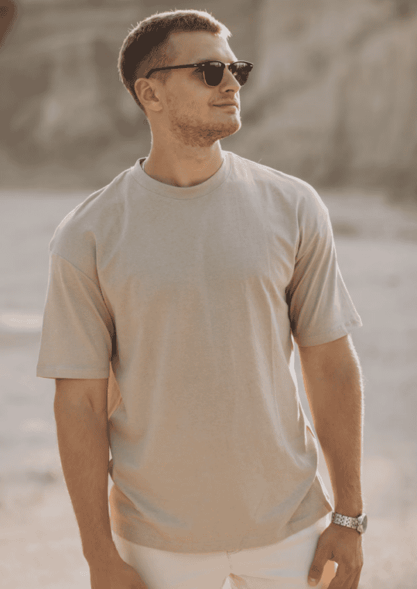 Homme portant un t-shirt beige avec lunettes de soleil, look estival décontracté et moderne en extérieur